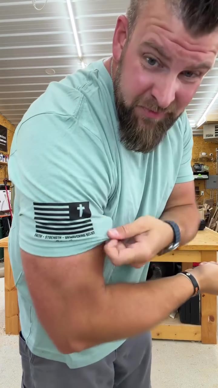 Bigger man pinching the snug sleeve of a mint Patriot Crew tee